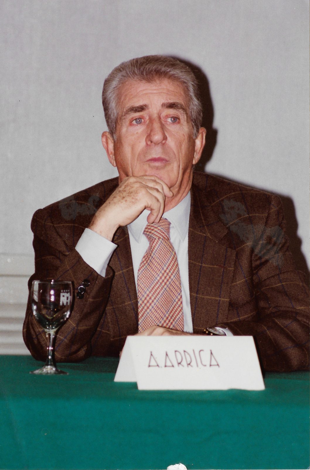 Arrica seduto al tavolo dei relatori dietro il segnaposto con il suo nome