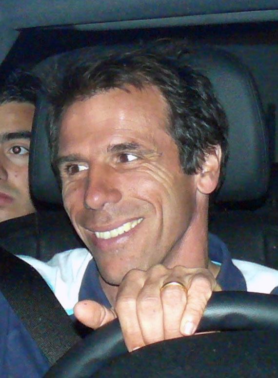 Gianfranco Zola sorridente alla guida di un'auto mentre firma autografi
